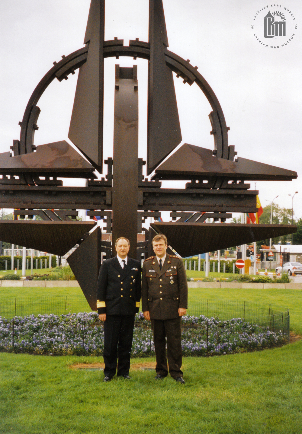 NBS komandieris viceadmirālis G. A. Zeibots un komandiera militārais pārstāvis NATO brigādes ģenerālis G. Ābols pie NATO emblēmas. Brisele, 2004. gads. Fotogrāfs nav zināms. LKM krājums