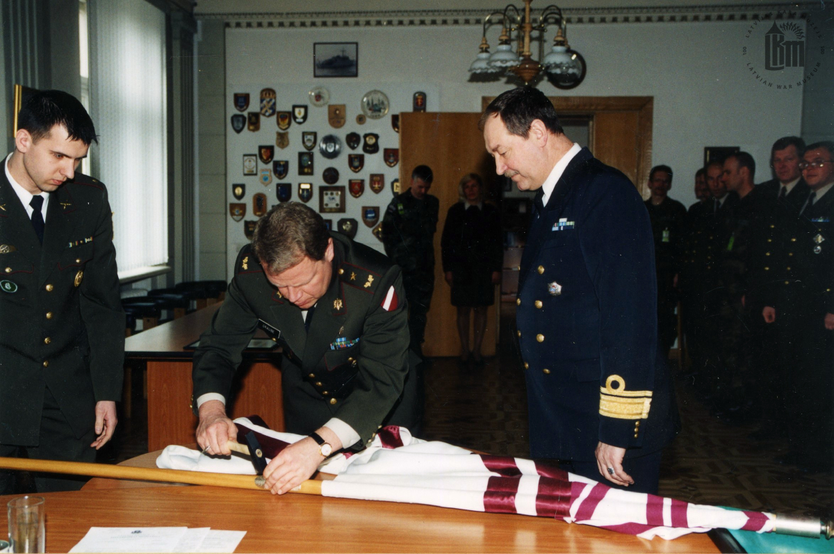 NBS komandieru maiņas ceremonija. NBS komandieris brigādes ģenerālis R. Graube iedzen NBS komandiera karoga kātā Karoga naglu.  2003. gada 30. janvāris. Fotogrāfs G. Binde. LKM krājums